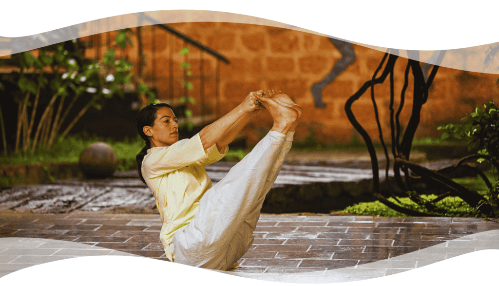 A yoga practitioner performing an Angamardana posture on a stone floor in a serene natural setting, symbolizing strength, agility, and balance through classical Hatha Yoga.