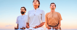 Three people seated in meditation posture practicing Bhastrika Kriya outdoors