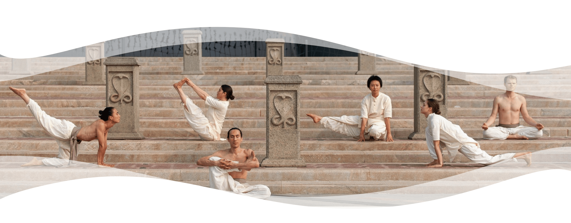 Group of Hatha Yoga practitioners in white clothing performing asanas and meditation on stone steps with carved pillars.